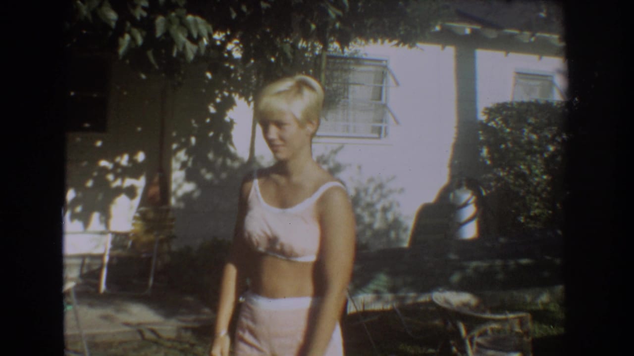 Blonde woman in a white two-piece swimsuit standing in a shaded backyard.