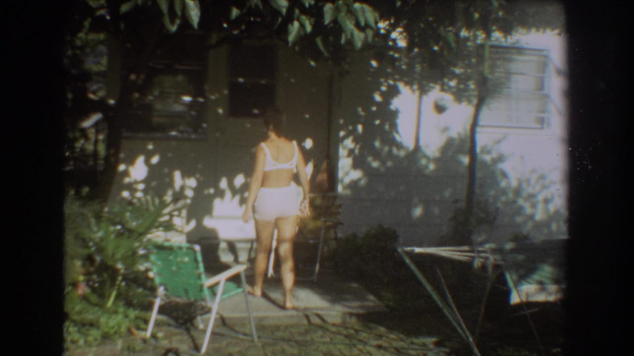 The woman moves farther into the shaded Fort Lauderdale backyard, framed by patio furniture, foliage, and the house exterior.