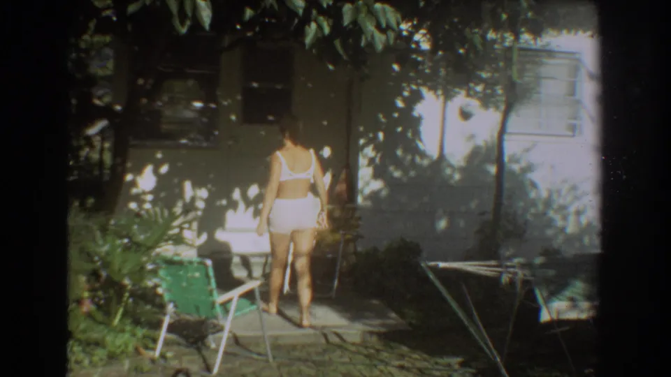 The woman moves farther into the shaded Fort Lauderdale backyard, framed by patio furniture, foliage, and the house exterior.