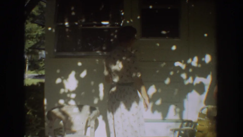 A woman in a floral dress stands outside a Fort Lauderdale vacation home, partly obscured by tree shade and 8mm exposure changes.