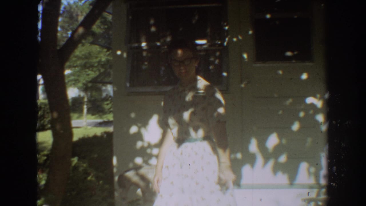 A woman wearing glasses is visible beside the Fort Lauderdale vacation home, framed by trees, porch chairs, and mottled sunlight.