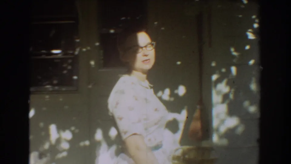 The woman with glasses turns beside a shaded residential doorway in Fort Lauderdale, with dappled light across the wall.