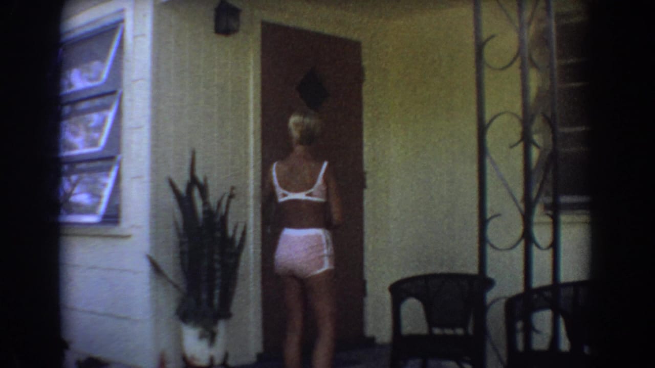 In 1967 Fort Lauderdale home-movie footage, a blonde woman in pink clothing faces a front door near a jalousie window and porch plants.