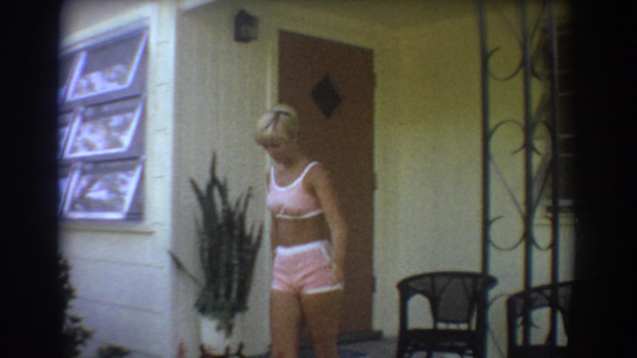 The woman stands in front of a Fort Lauderdale house exterior, with a window, door, porch chairs, and plants visible around her.
