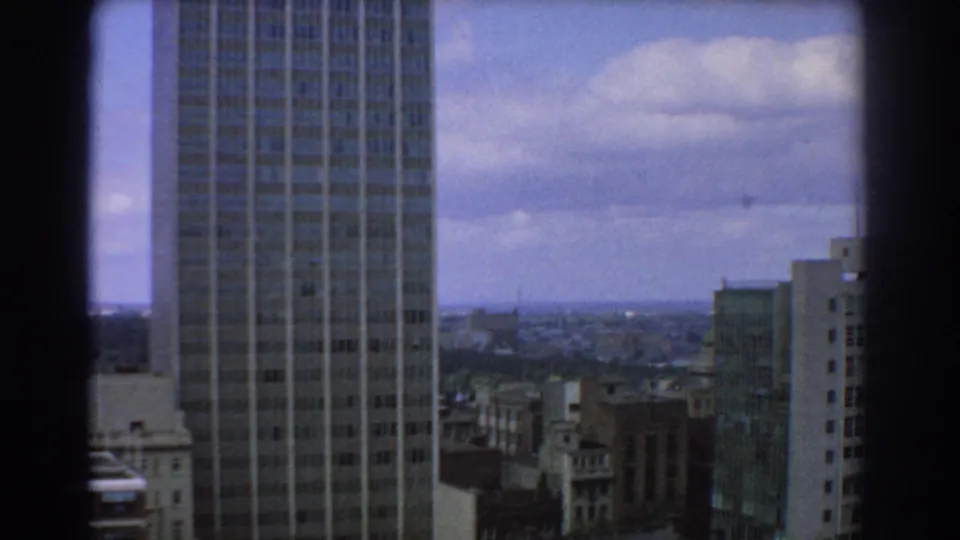 1967 Melbourne skyline frame with a tall modern tower at left, mid-century buildings, and distant urban blocks below clouds.