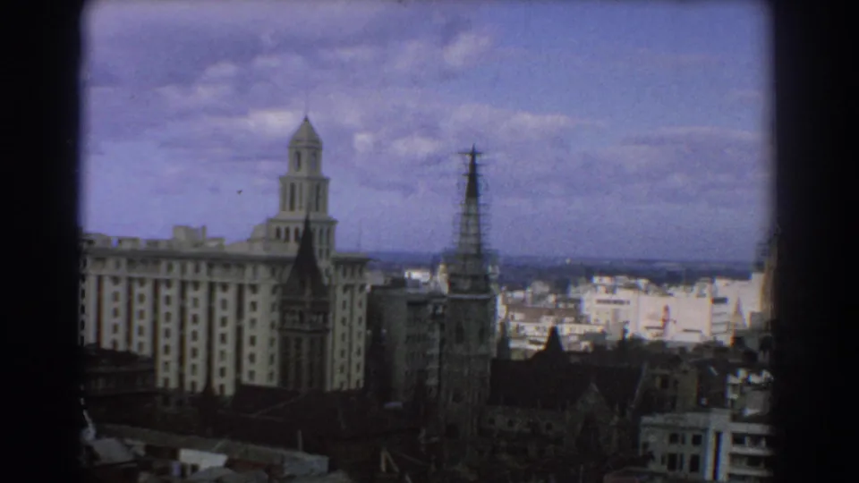 1967 Melbourne view showing older masonry buildings, church spires, lower city blocks, and a broad cloudy sky.
