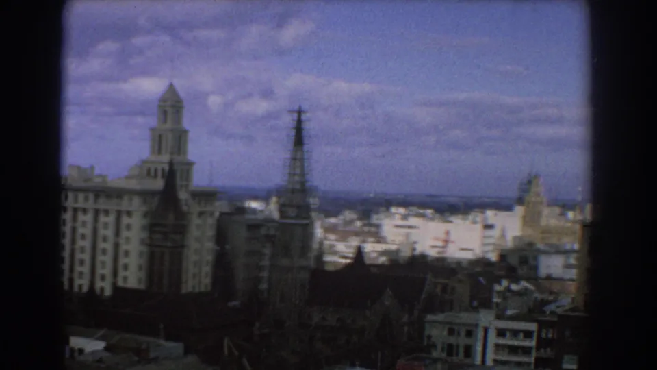 1967 Melbourne skyline with prominent church spires, older buildings in the foreground, and bright distant city blocks.
