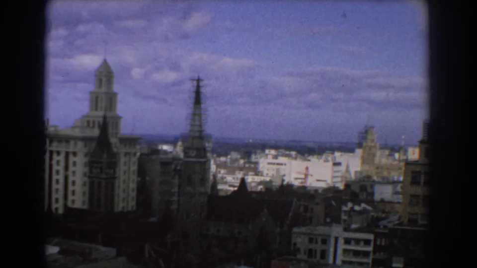 1967 Melbourne city view with a church spire, pale towered building, clustered rooftops, and soft 8mm vignetting.