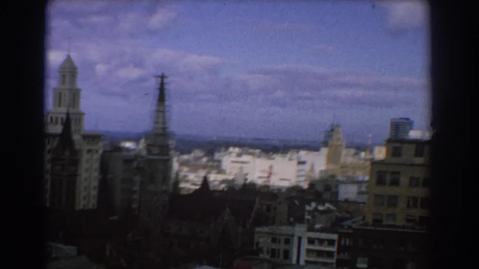 1967 Melbourne skyline showing a church spire, rooftop antenna tower, pale commercial buildings, and blue sky.
