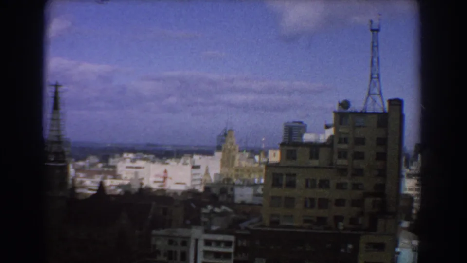 1967 Melbourne cityscape with a rooftop antenna mast, mid-rise block, pale downtown buildings, and 8mm edge darkening.