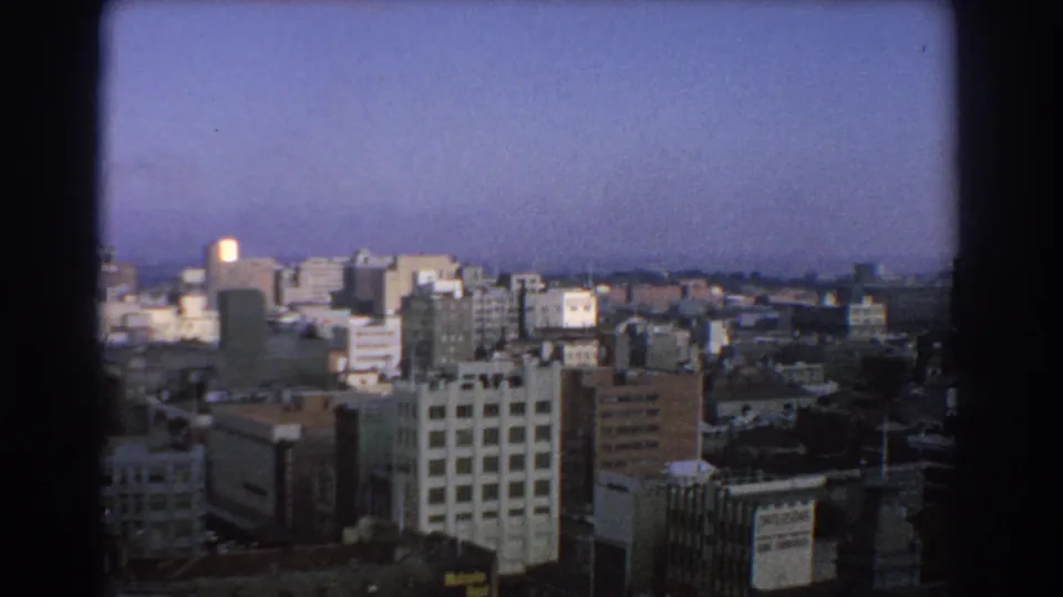Melbourne skyline from an elevated position, showing clustered office buildings, distant horizon, and dark 8mm frame edges.