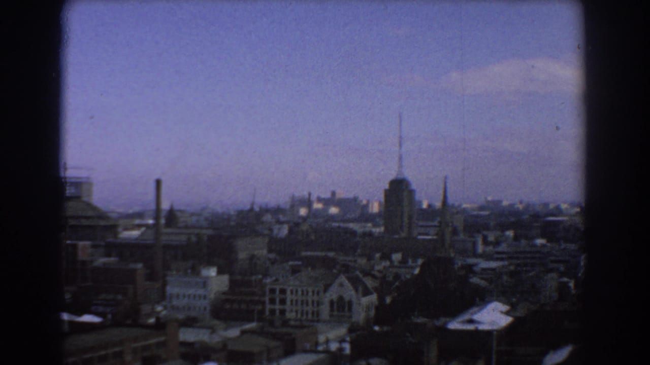 Melbourne skyline seen through dark window framing under a blue-purple sky.