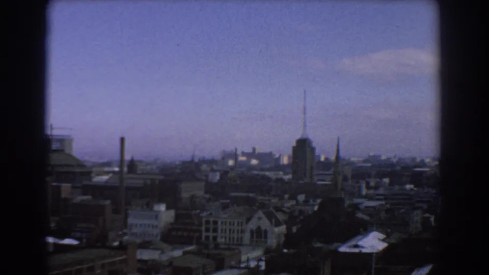 A 1967 Melbourne city view framed by dark vertical trim, showing low-rise buildings, church spires and an antenna-topped tower.