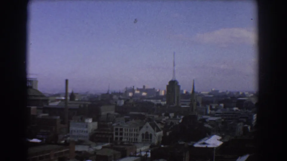 End frame of a 1967 Melbourne skyline view, with dark window trim, low city buildings, spires and an antenna-topped tower.
