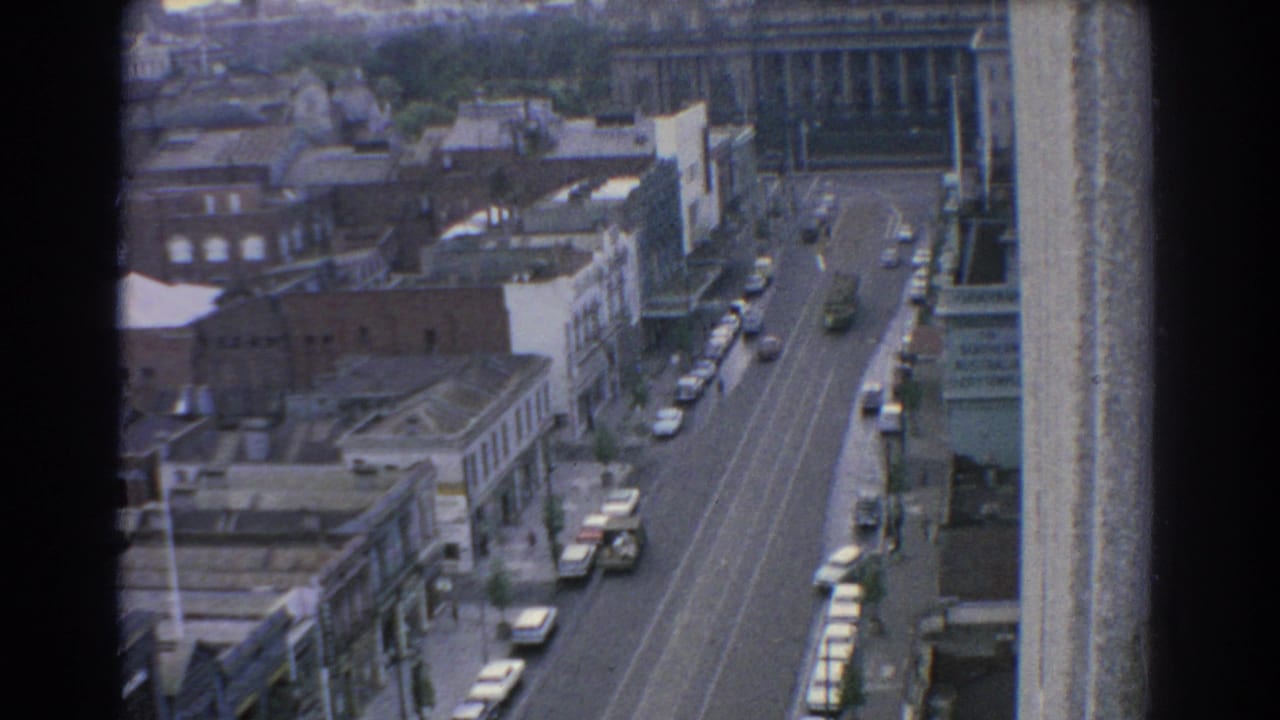 Elevated view down a city street with cars, rooftops, and mid-century buildings.