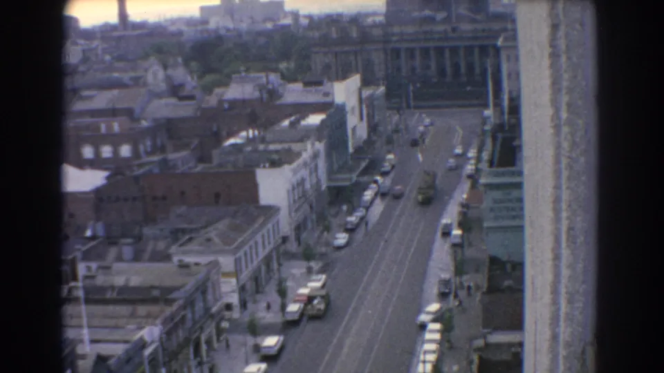 Elevated 1967 Melbourne street view showing cars on a broad roadway, low urban buildings, and a hazy skyline beyond.