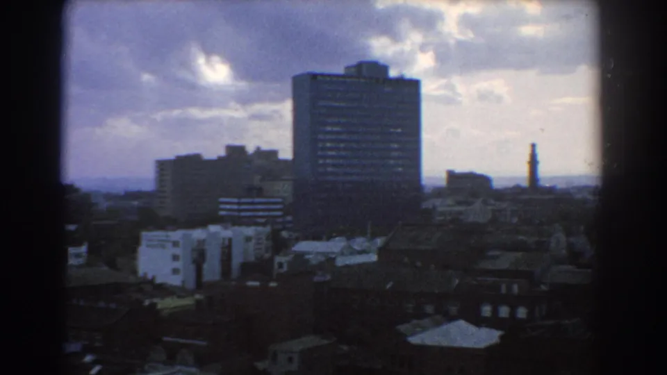 Melbourne skyline during a slow pan, showing a prominent rectangular high-rise, lower buildings, trees, and cloud breaks.