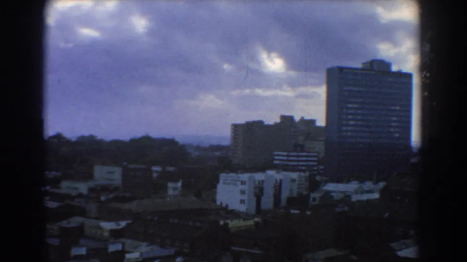 1967 Melbourne panoramic view with office towers, residential rooftops, tree cover, distant horizon, and moody cloud cover.