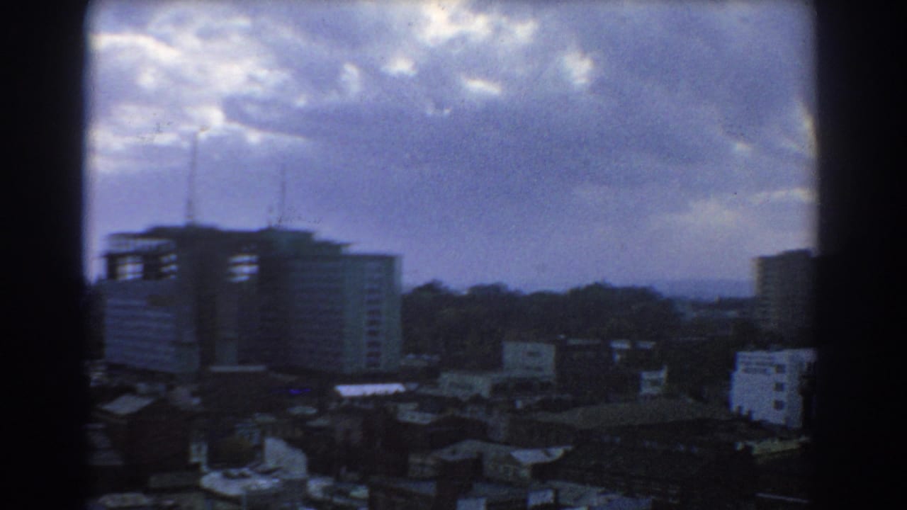 1967 Melbourne cityscape from an elevated viewpoint, showing low rooftops, a prominent mid-rise building, antennas, and heavy cloud cover.