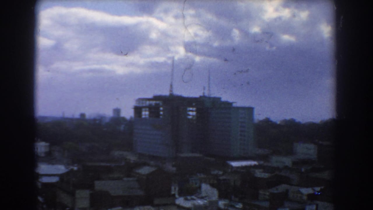 Clouds over a distant urban skyline with a large building and antennas in the middle distance.