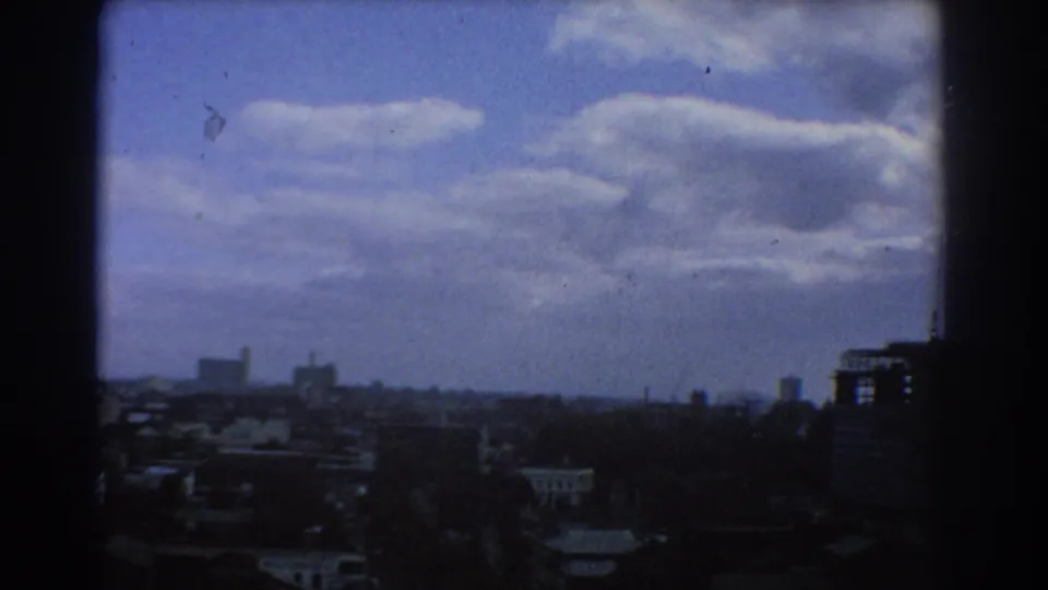 Elevated Melbourne city view from 1967, showing low urban buildings, a distant horizon, scattered taller structures, and a sky filled with large clouds.