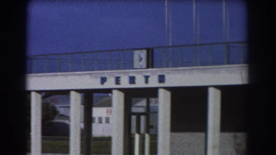 1967 home-movie view of the Perth Airport terminal facade, with large PERTH lettering, glass, columns, and dark 8mm frame edges.