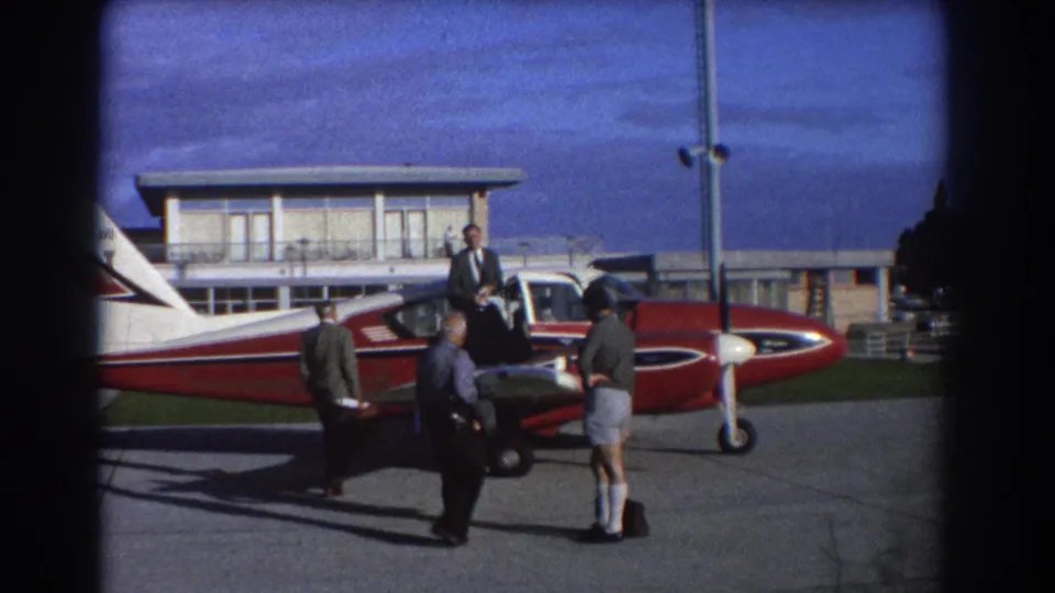 A man boards the red and white propeller aircraft as other men stand on the Perth Airport tarmac in 1967 home-movie footage.