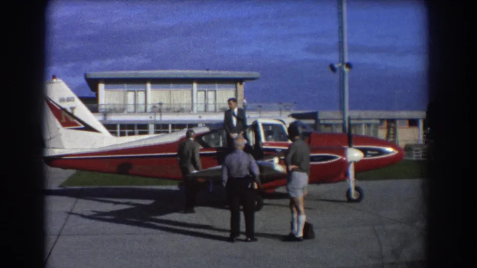 A suited man stands at the open aircraft door while three men wait beside the small red and white plane at Perth Airport.
