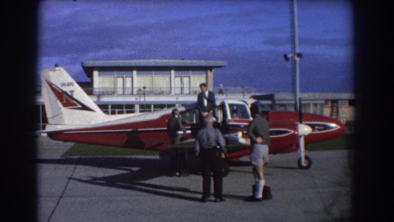 Men gathered beside a red and white single-engine aircraft on an airport apron.