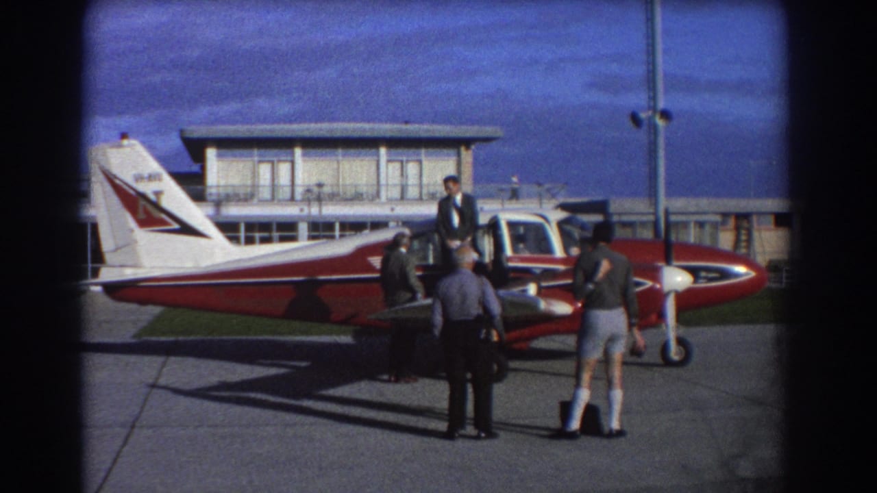 Group of men standing near the nose and cockpit of a red and white aircraft.