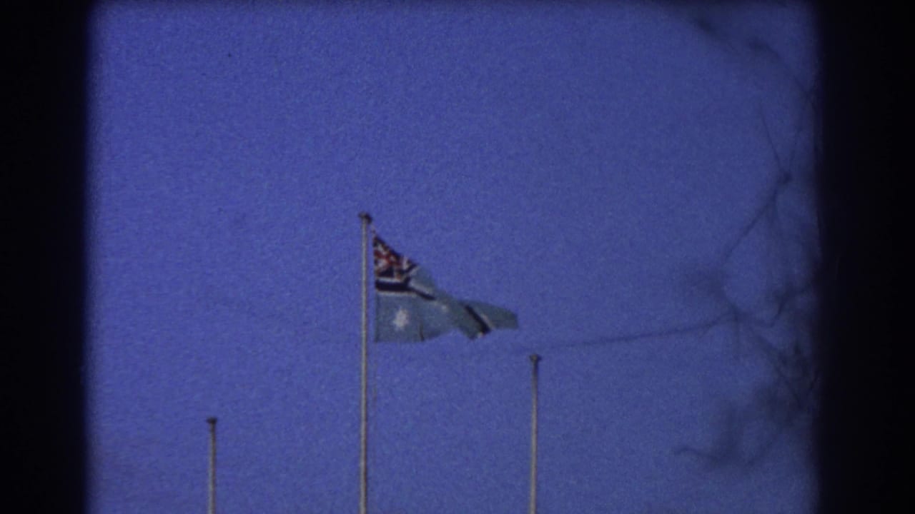 Australian flag fluttering on a pole with empty flagpoles nearby and dark film edges.