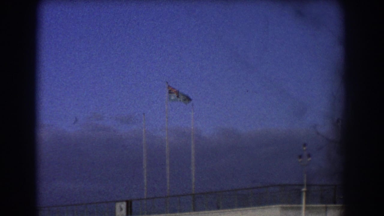 Flag on a tall pole above an airfield building under a deep blue sky.