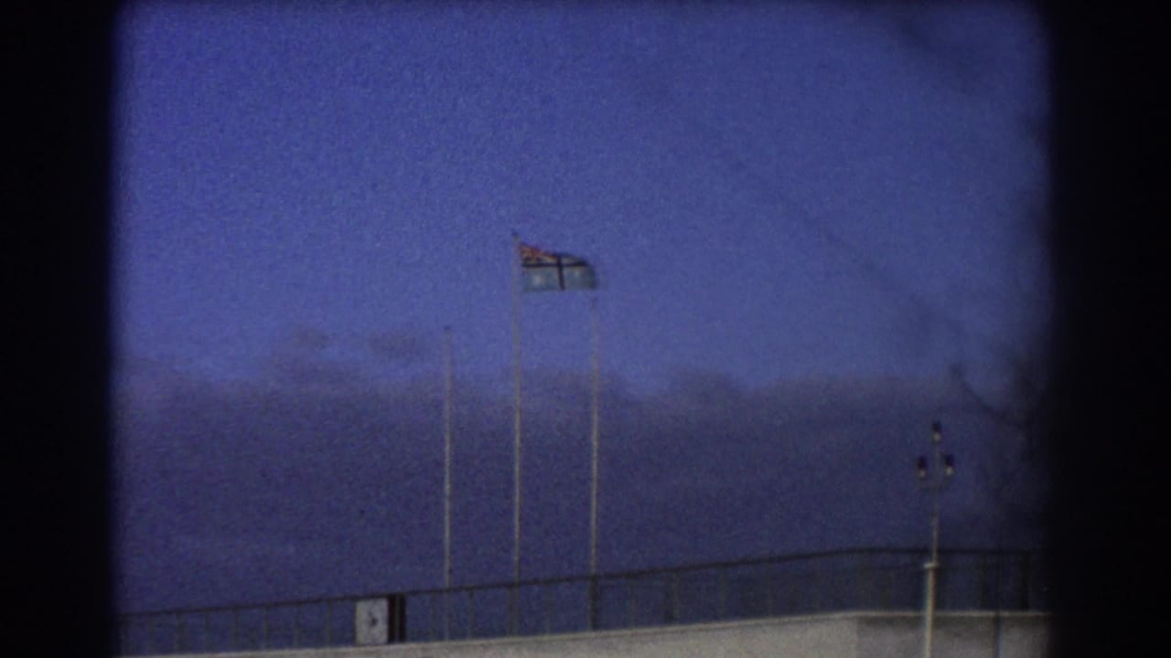 Flag and poles above a low airfield building against a blue sky.