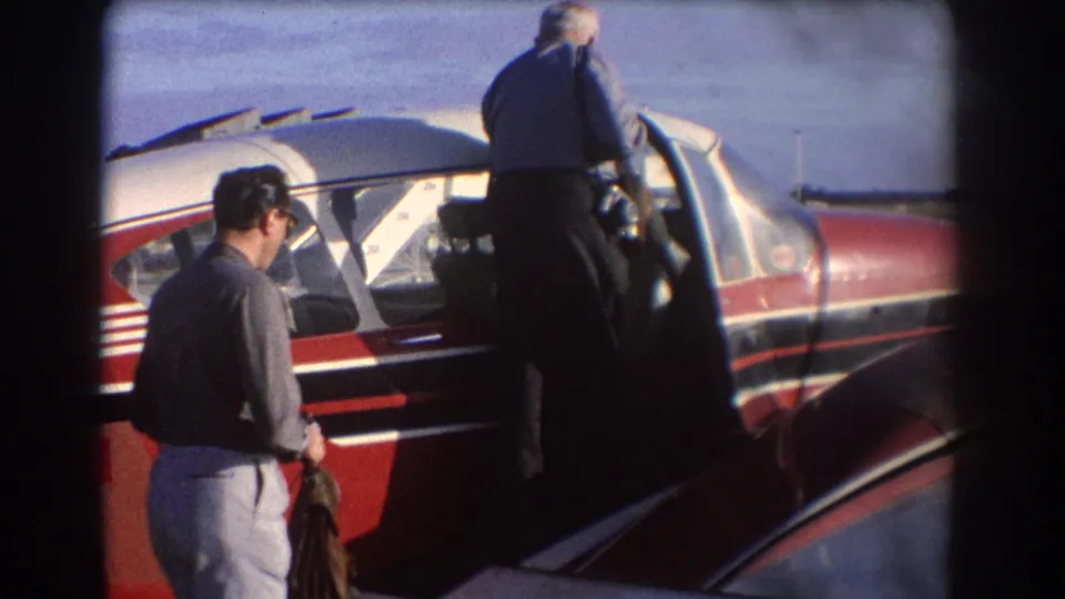 A man boards or stands at the open door of a red and white small aircraft while another man with luggage watches in the 1967 Perth footage.