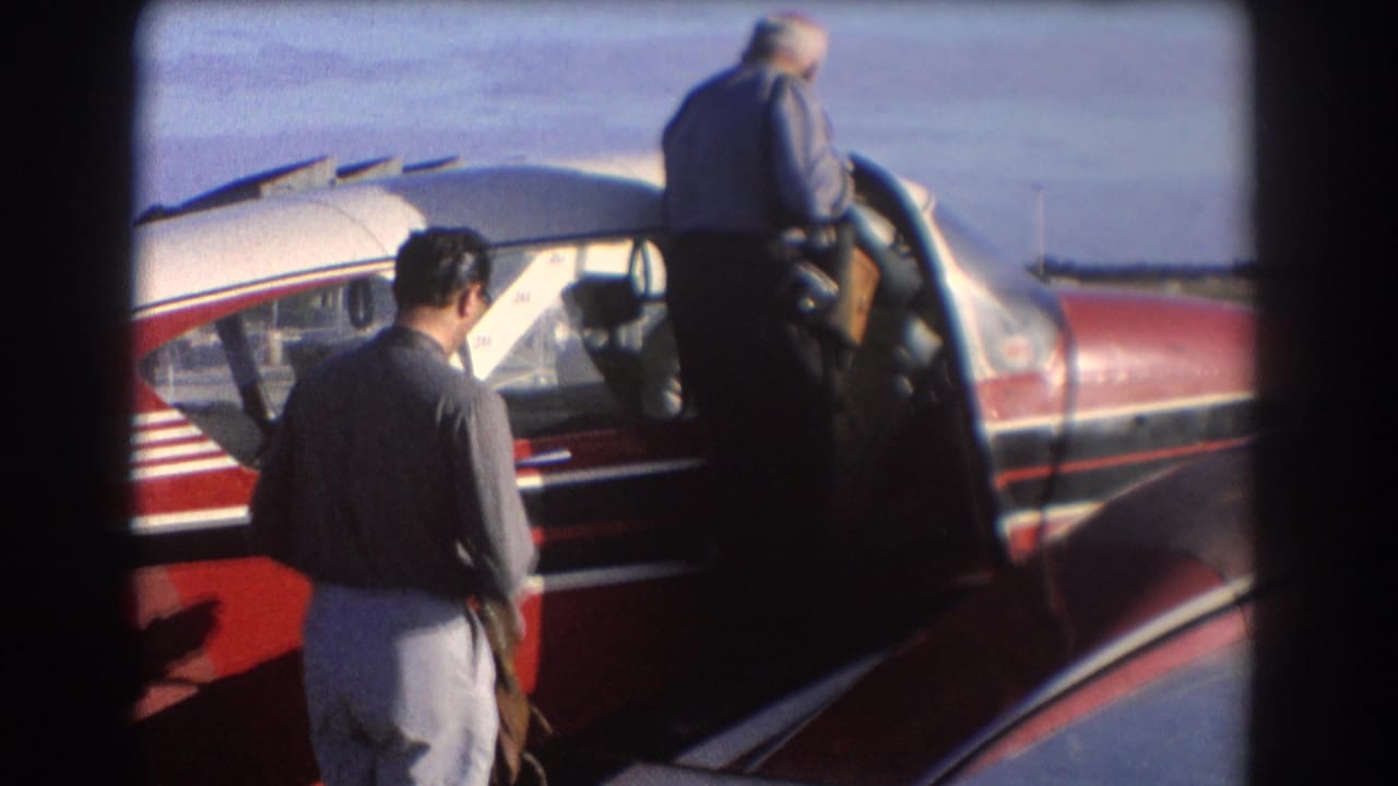 Two people stand beside a red-and-white small aircraft with an open cabin door.