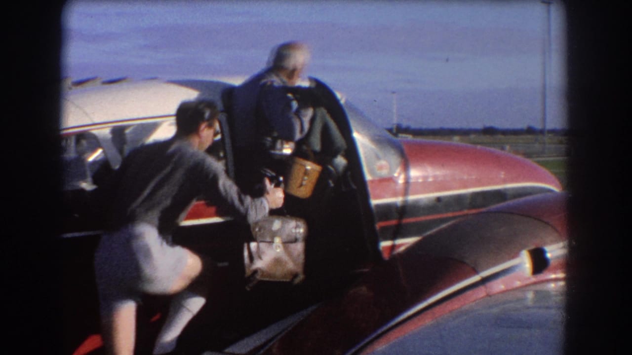 A man hands luggage toward another person entering a small red aircraft.