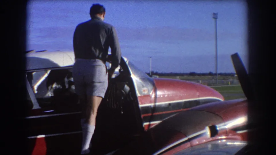 1967 Perth frame showing a man at the open cabin of a red-and-white private plane under a blue sky.