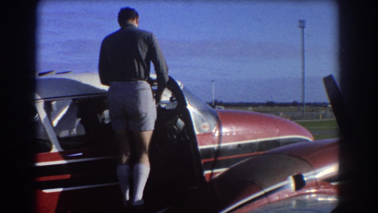 Man in dark shirt and light shorts stands beside an open small aircraft door.