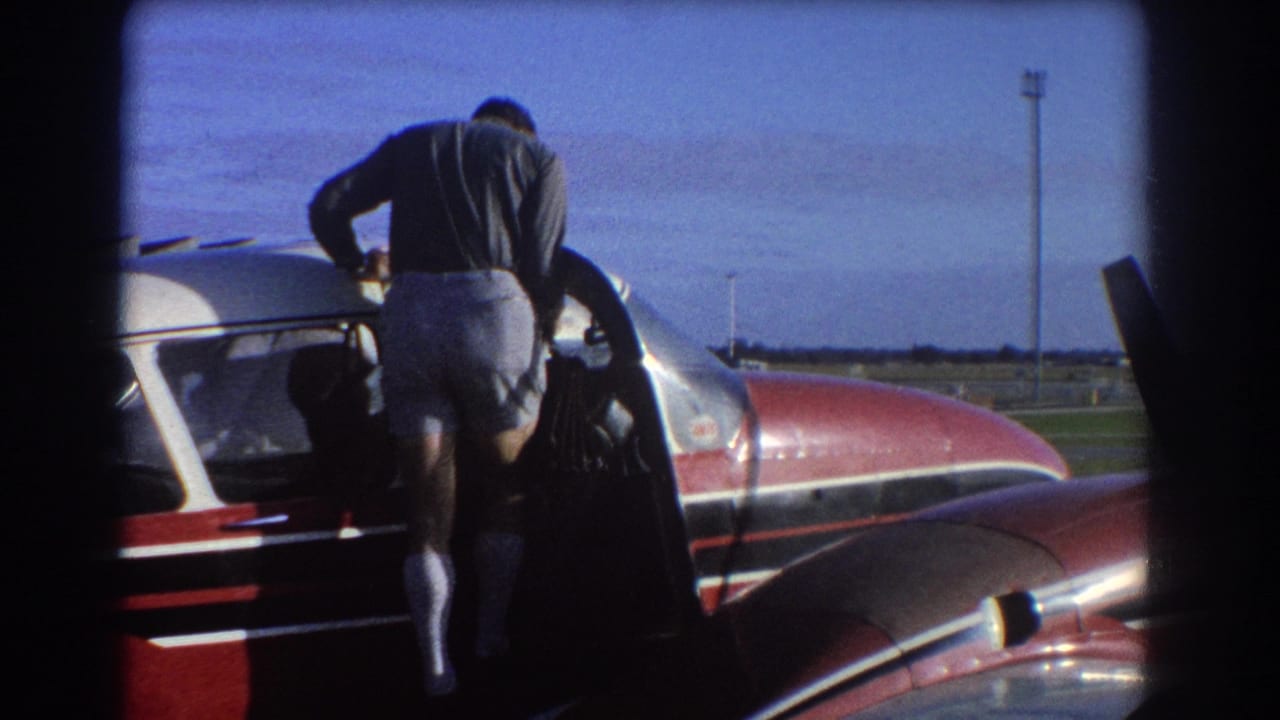 Man leans into the open side door of a red and white small aircraft.