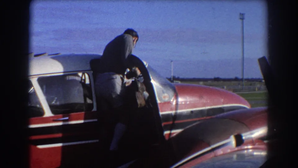 The man steps into the red and white small aircraft while the camera watches from outside on the Perth airfield.