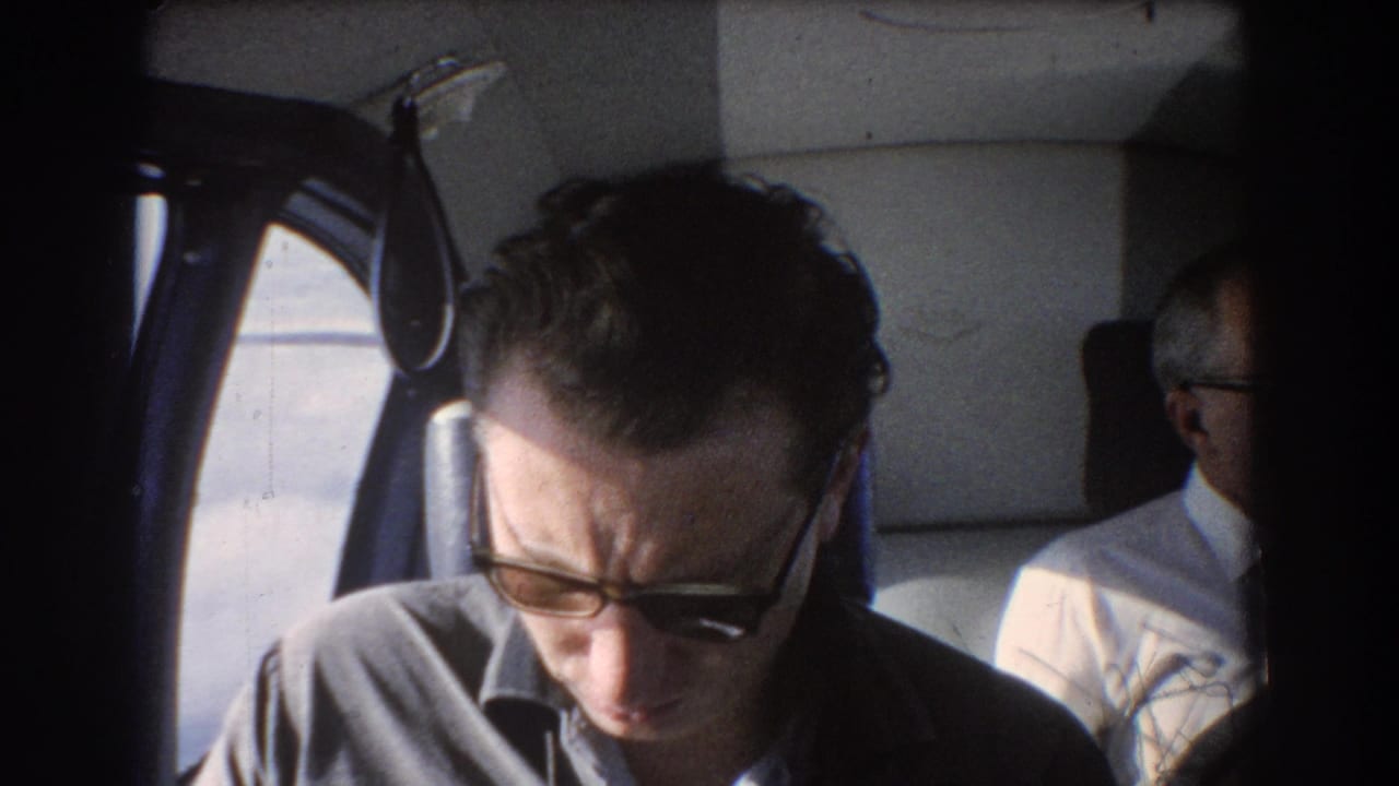1967 Perth, Australia travel footage showing a man in sunglasses reading in an airplane cabin, with another passenger in the background.