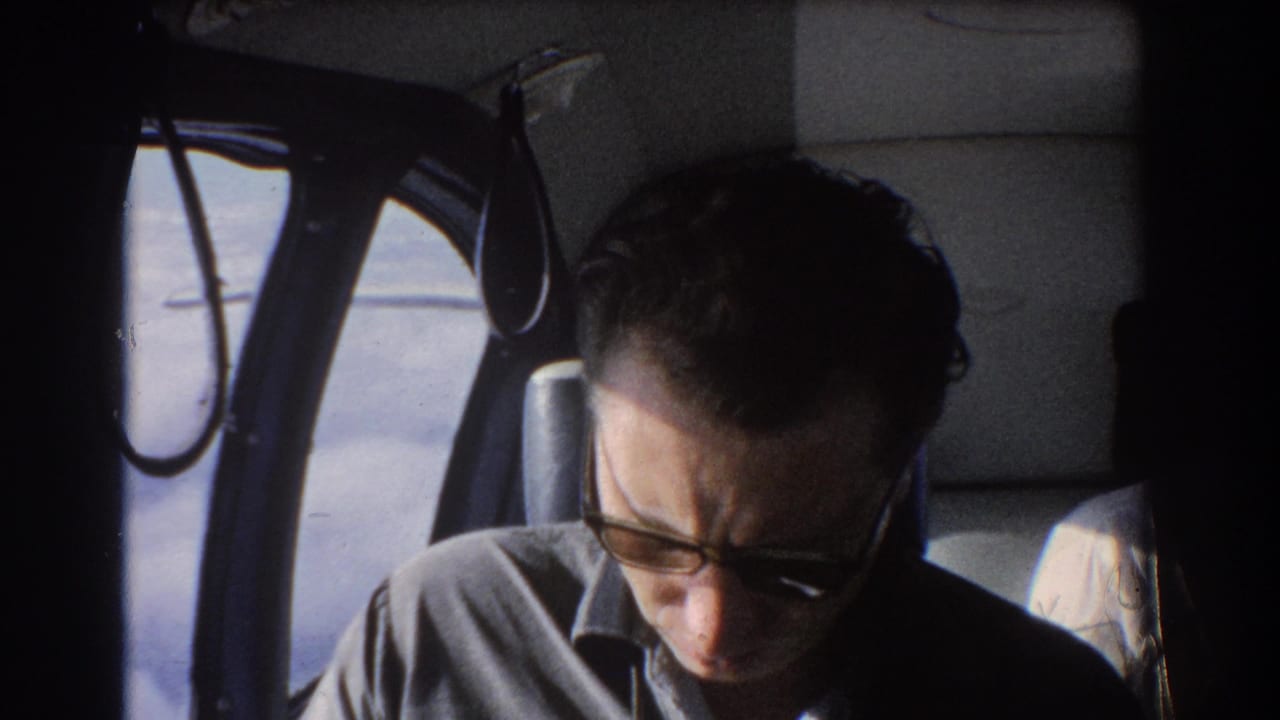 Man reading beside an airplane window, partially framed by dark cabin trim.