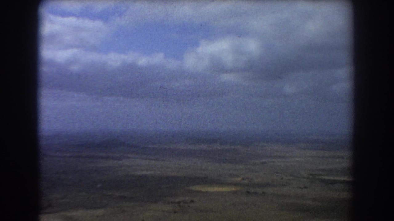Cloudy sky and arid land seen through dark aircraft window framing.