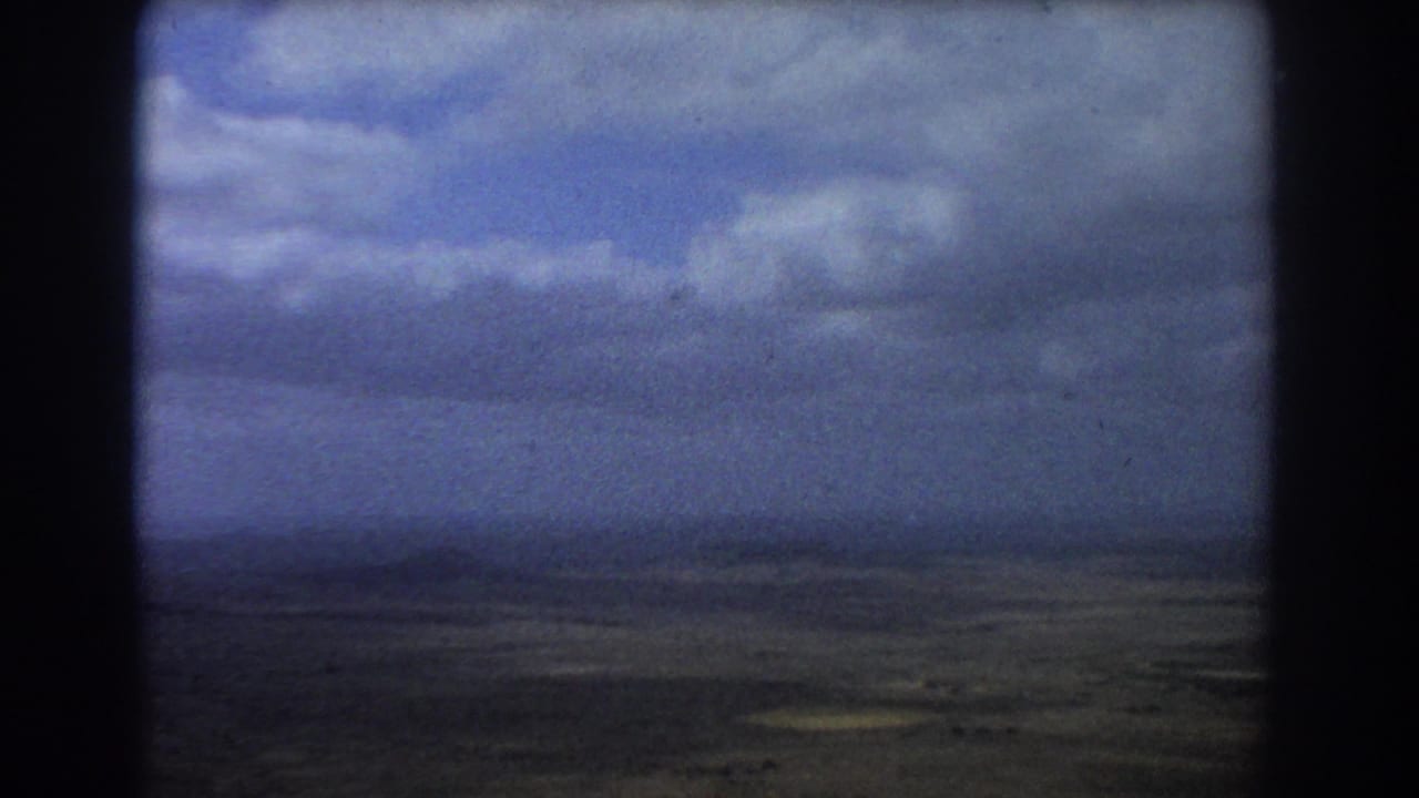 Aerial landscape under clouds divided by dark aircraft interior framing.