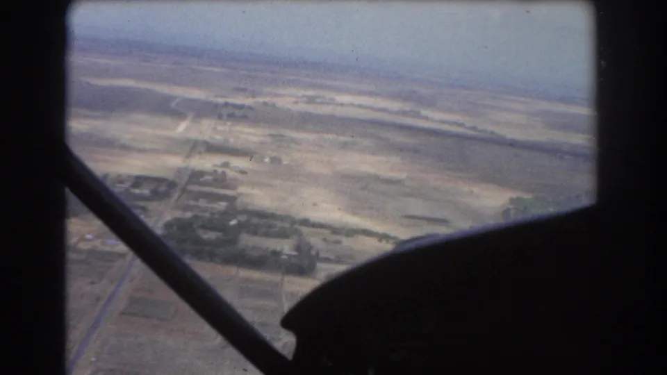 1967 8mm aerial view near Perth showing pale dry fields, road lines, and a dark aircraft strut in the foreground.