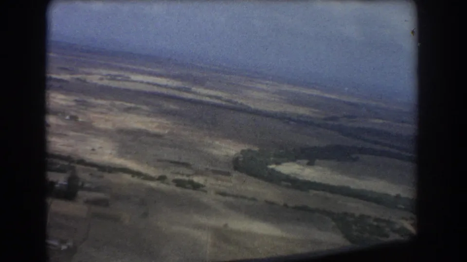 Passenger aerial view near Perth, Australia, showing dry terrain, scattered green patches, and aircraft window framing on 8mm film.