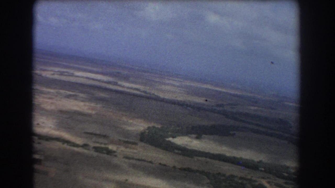 Tilted aerial view over flat plains and pale waterways through an airplane window.