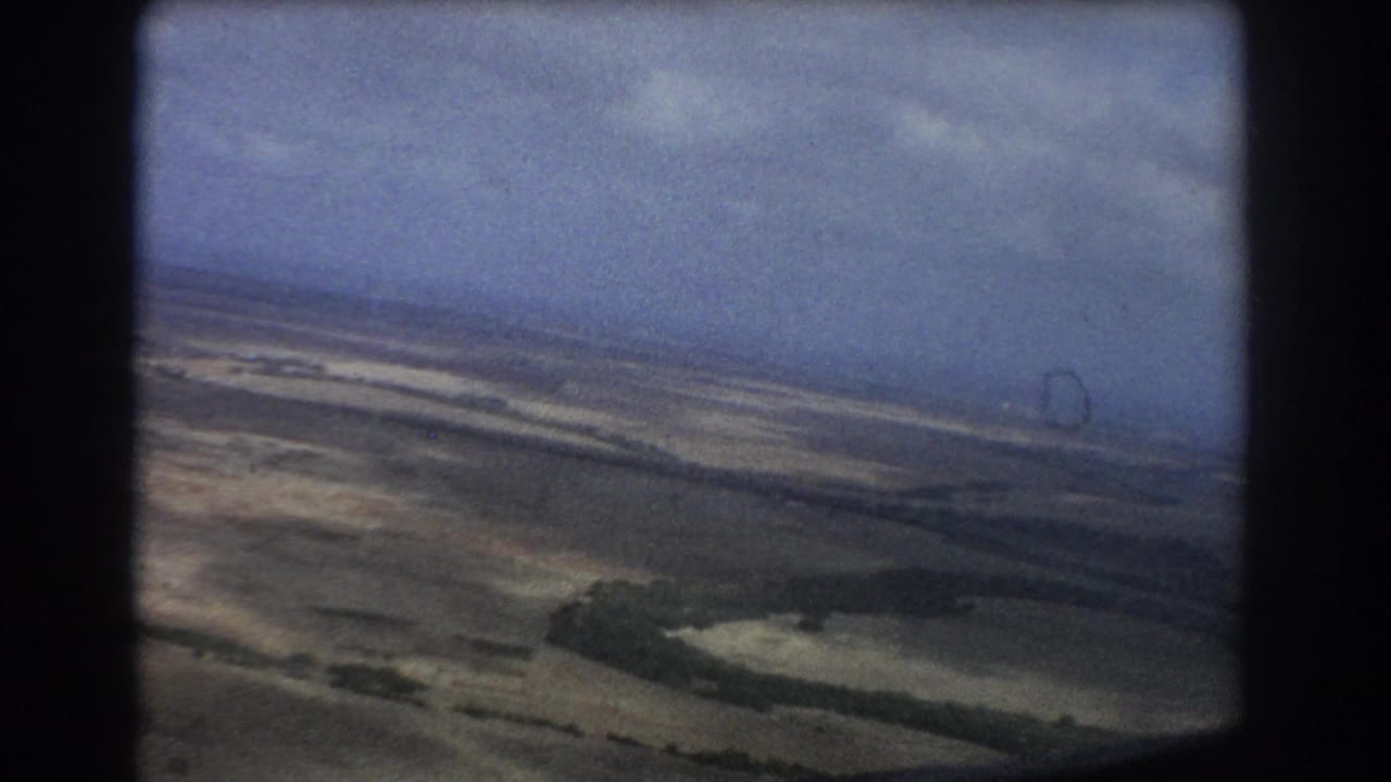 Aerial landscape with fields, winding pale lines, and dark window framing.
