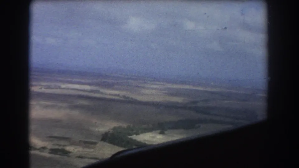 Vintage 8mm aerial view near Perth, with flat land, cloudy sky, and a dark aircraft or window edge entering the lower foreground.