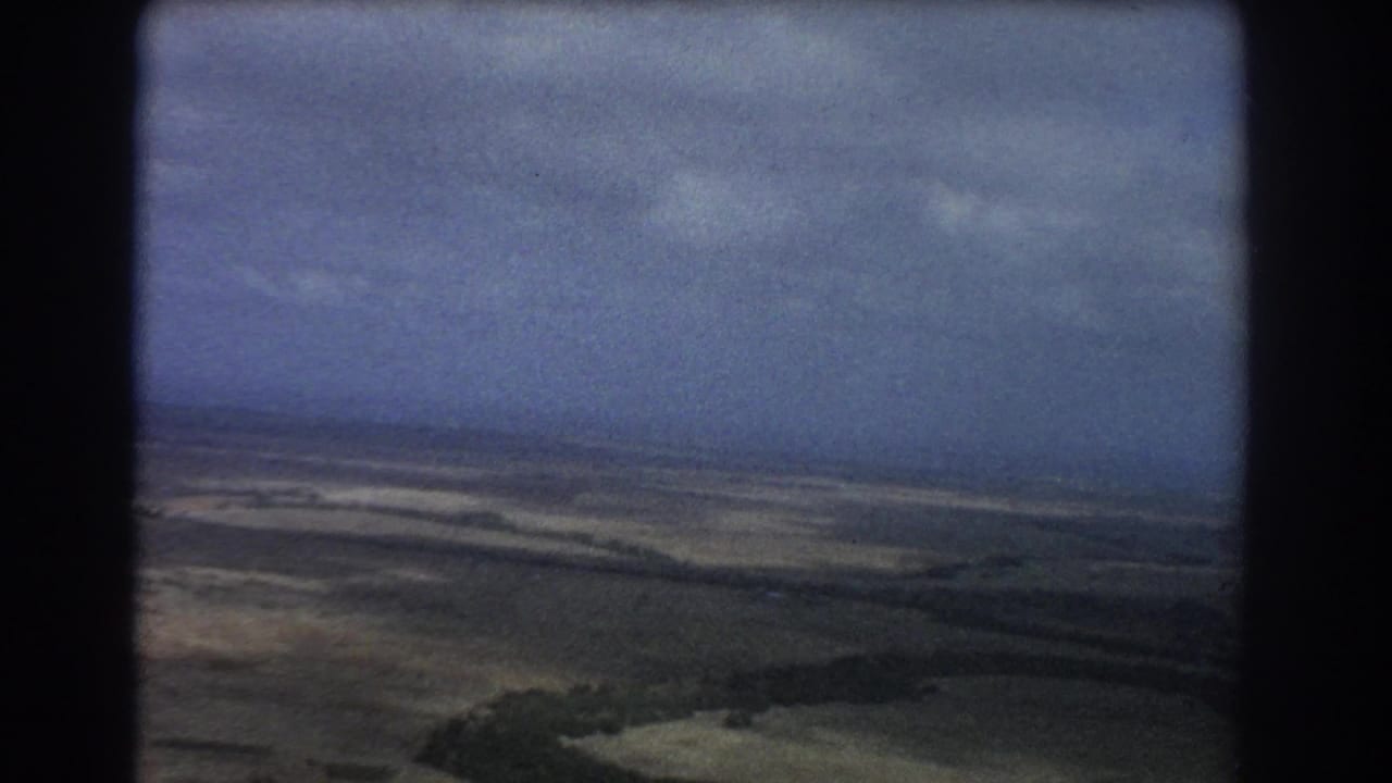 Aerial view of dry landscape and low hills seen through a dark aircraft window frame.